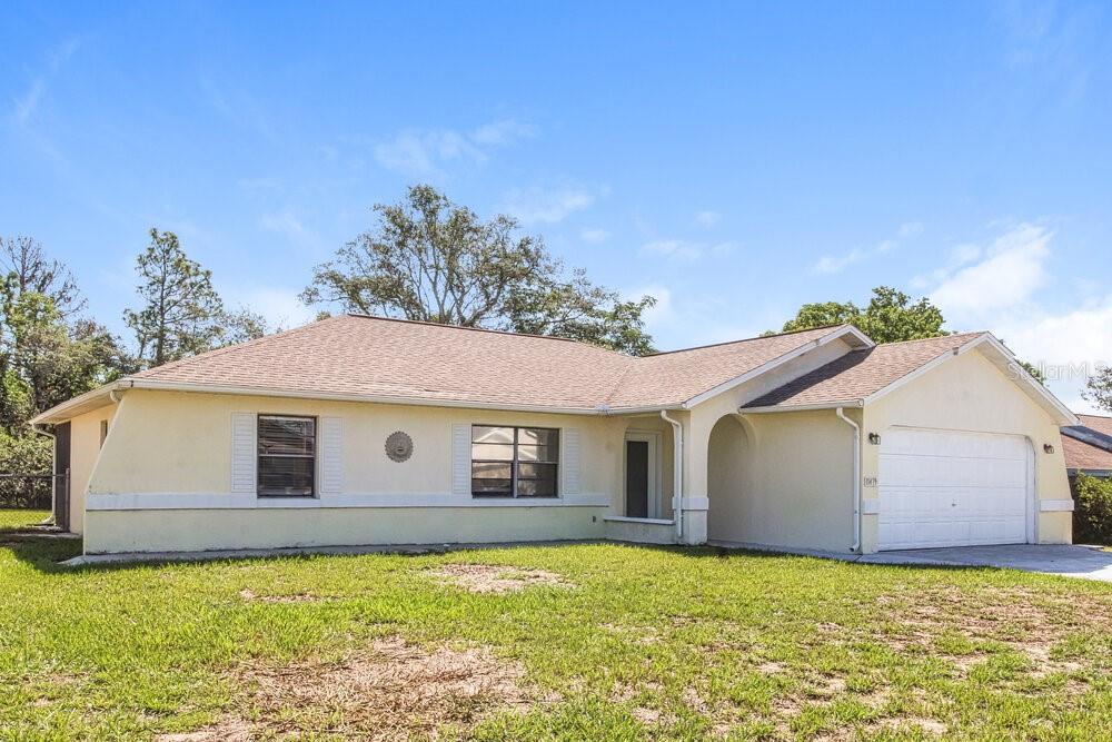 A single-story house with light yellow stucco, a brown shingled roof, and an attached garage — 11479 CAVERN ROAD, SPRING HILL, FL