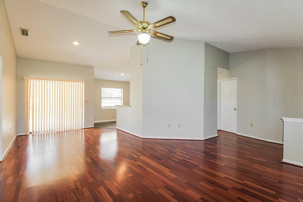 An empty living room features hardwood floors, a ceiling fan, and a sliding glass door — 11479 CAVERN ROAD, SPRING HILL, FL