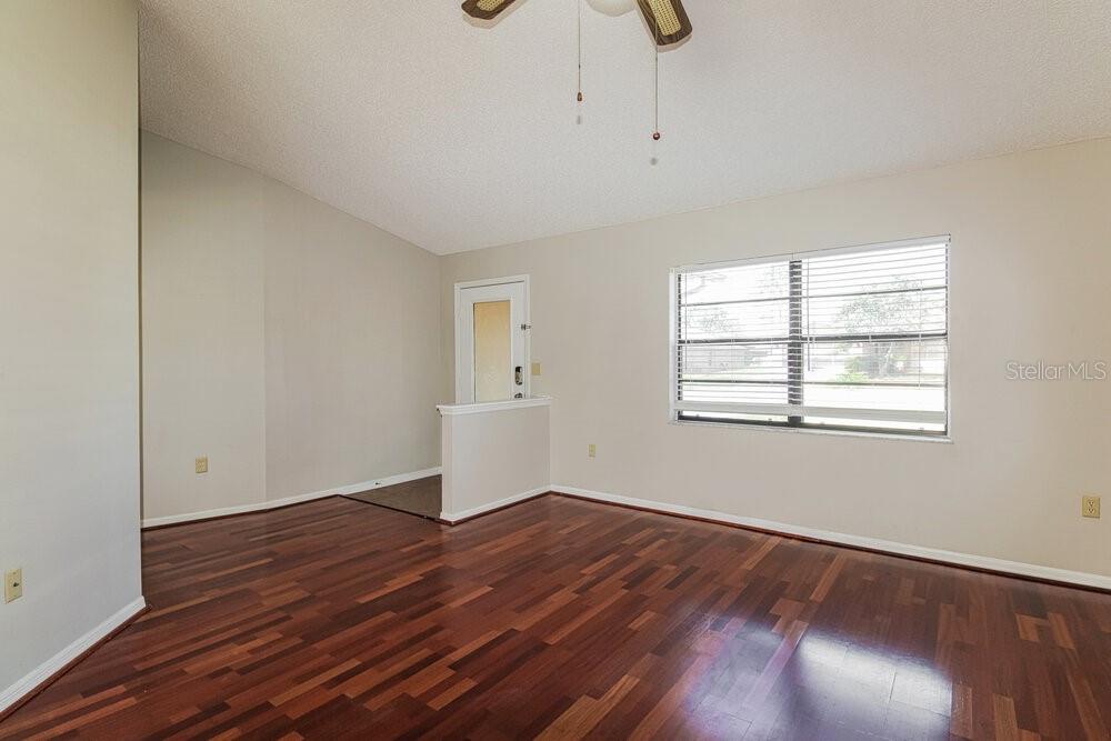 An empty room with dark hardwood floors, beige walls, and a window with white blinds — 11479 CAVERN ROAD, SPRING HILL, FL