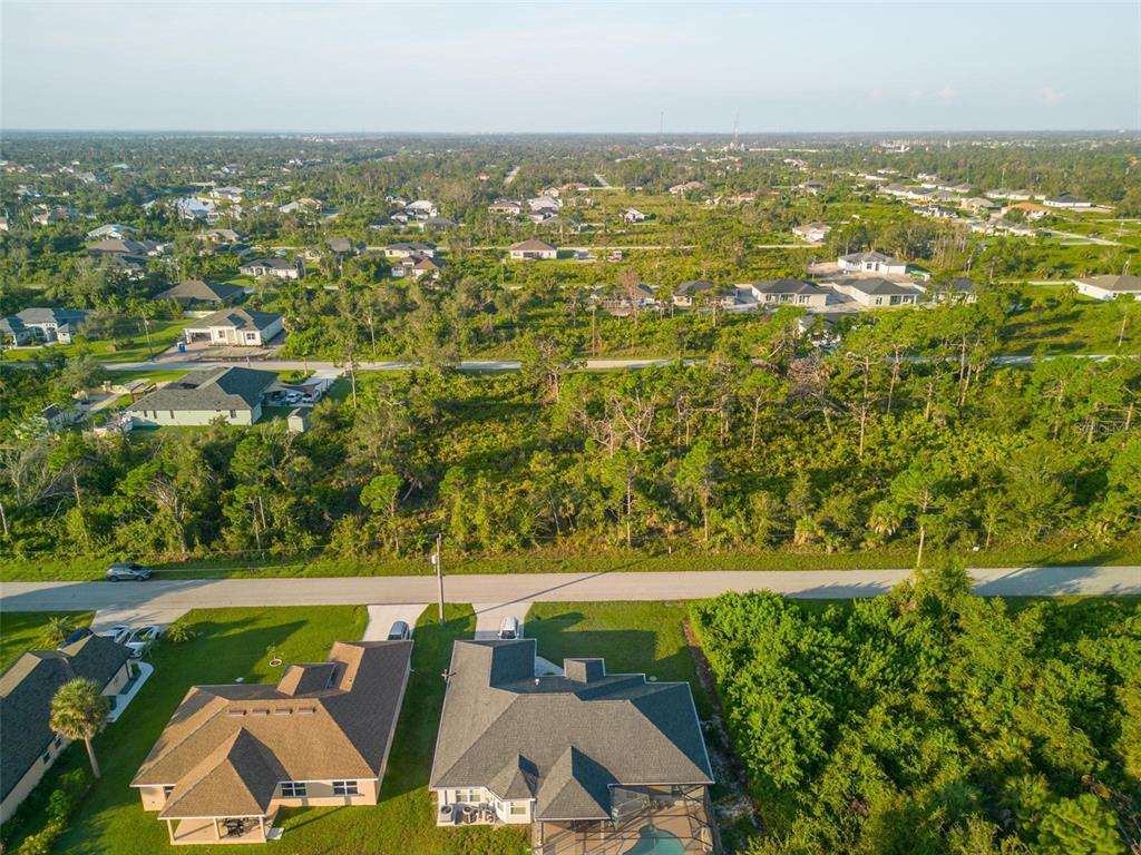 An aerial view shows two houses in the foreground with a large, wooded vacant lot behind — 13409 YAGER LANE, PORT CHARLOTTE, FL