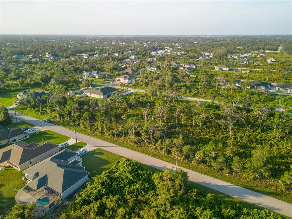 An aerial view shows a paved road winding through a residential area with wooded lots — 13409 YAGER LANE, PORT CHARLOTTE, FL