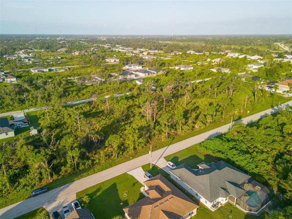 An aerial view shows a residential neighborhood with houses surrounded by dense, wooded vegetation — 13409 YAGER LANE, PORT CHARLOTTE, FL