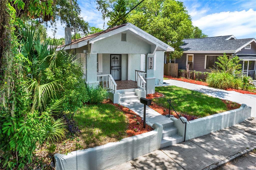 A light-colored bungalow with a front porch, a small yard, and a concrete retaining wall — 112 E EMILY STREET, TAMPA, FL