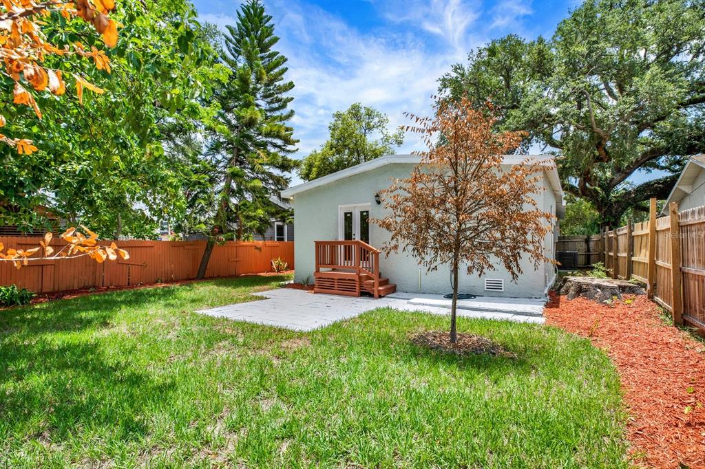 A backyard features a small house with a wooden deck, a patio, and a tree — 112 E EMILY STREET, TAMPA, FL
