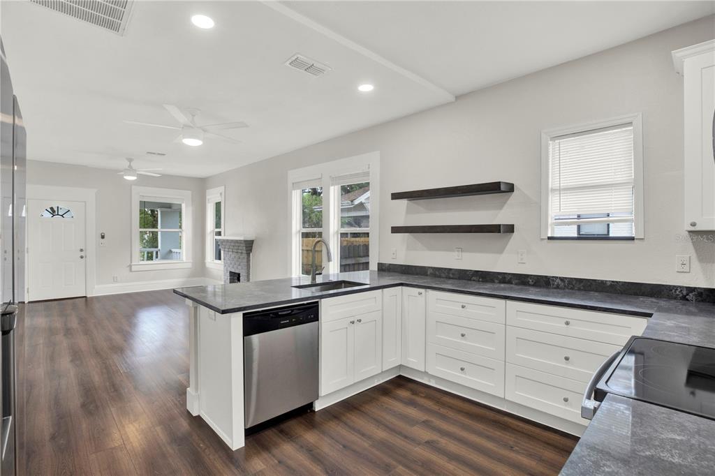 A kitchen with white cabinets, dark countertops, and open shelving overlooks a living area — 112 E EMILY STREET, TAMPA, FL