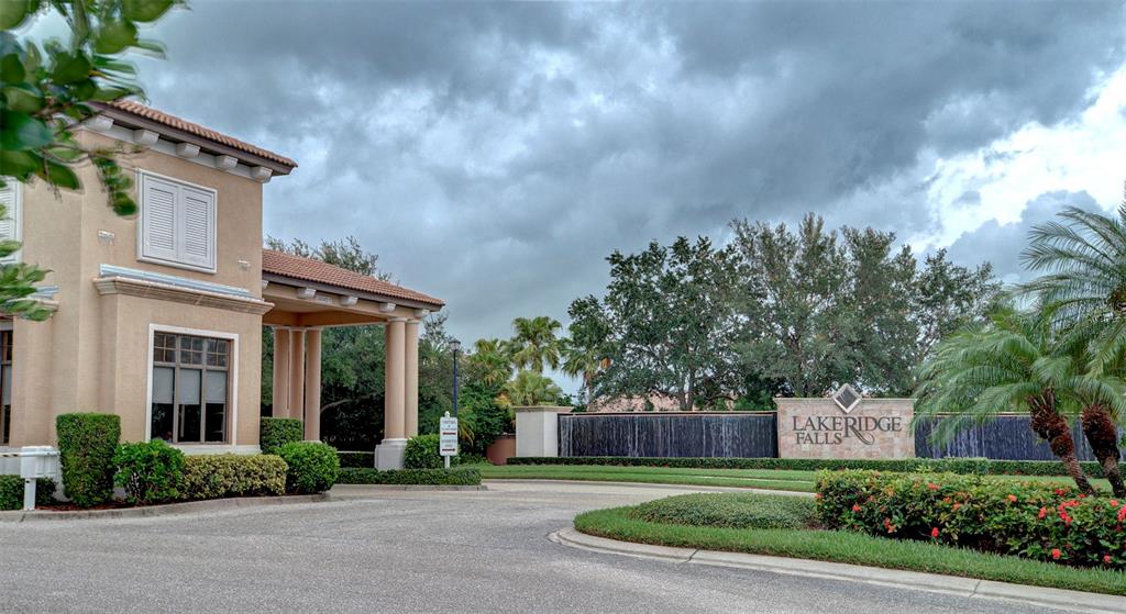 The entrance to Lakeridge Falls features a beige building, a waterfall sign, and palm trees — 4019 CASCADE FALLS DRIVE, SARASOTA, FL