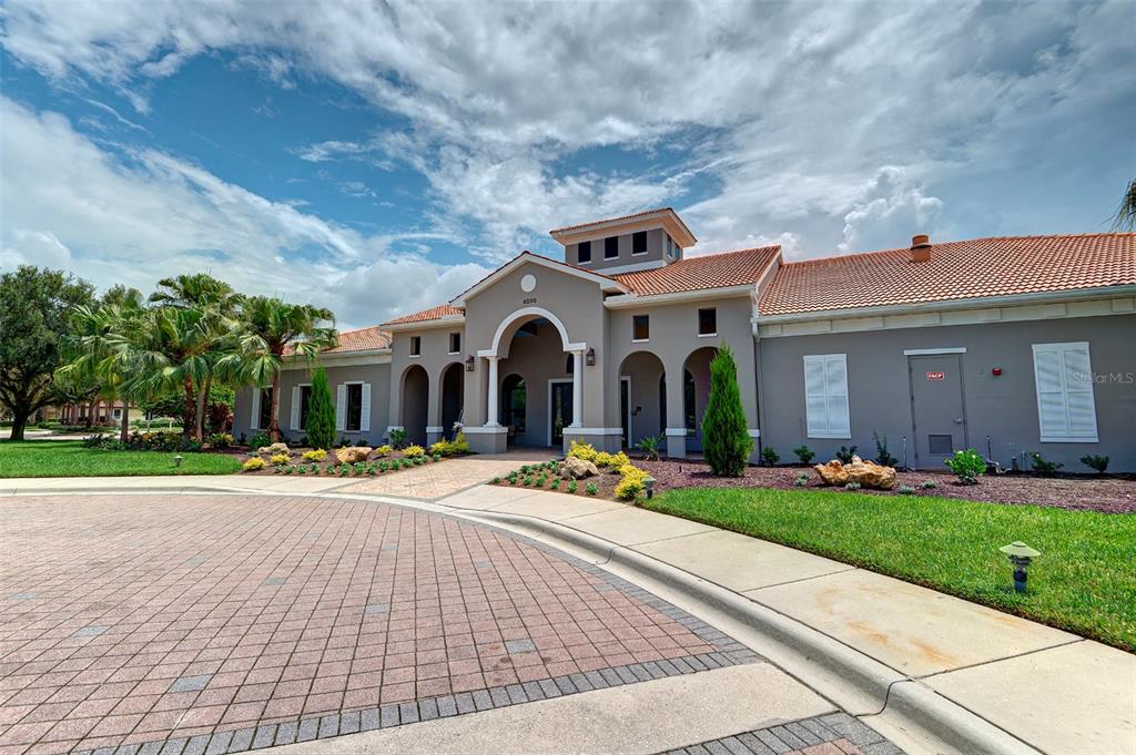 The exterior of a beige stucco community clubhouse features a tiled roof and arched entryway — 4019 CASCADE FALLS DRIVE, SARASOTA, FL