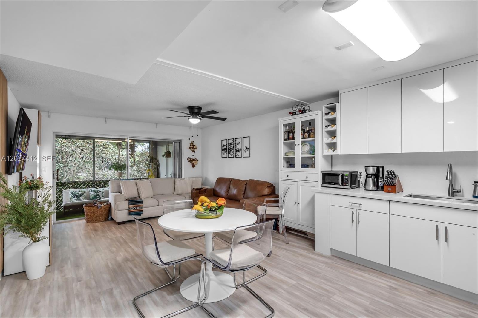 An open-concept living and dining area features white cabinets, a round table, and sliding doors — 420 NW 70th Ave # 228, Plantation FL 33317, PLANTATION, FL
