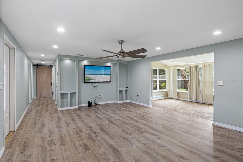 A living room features light blue walls, wood-look flooring, a ceiling fan, and built-in shelving — 3831 118TH STREET W, BRADENTON, FL