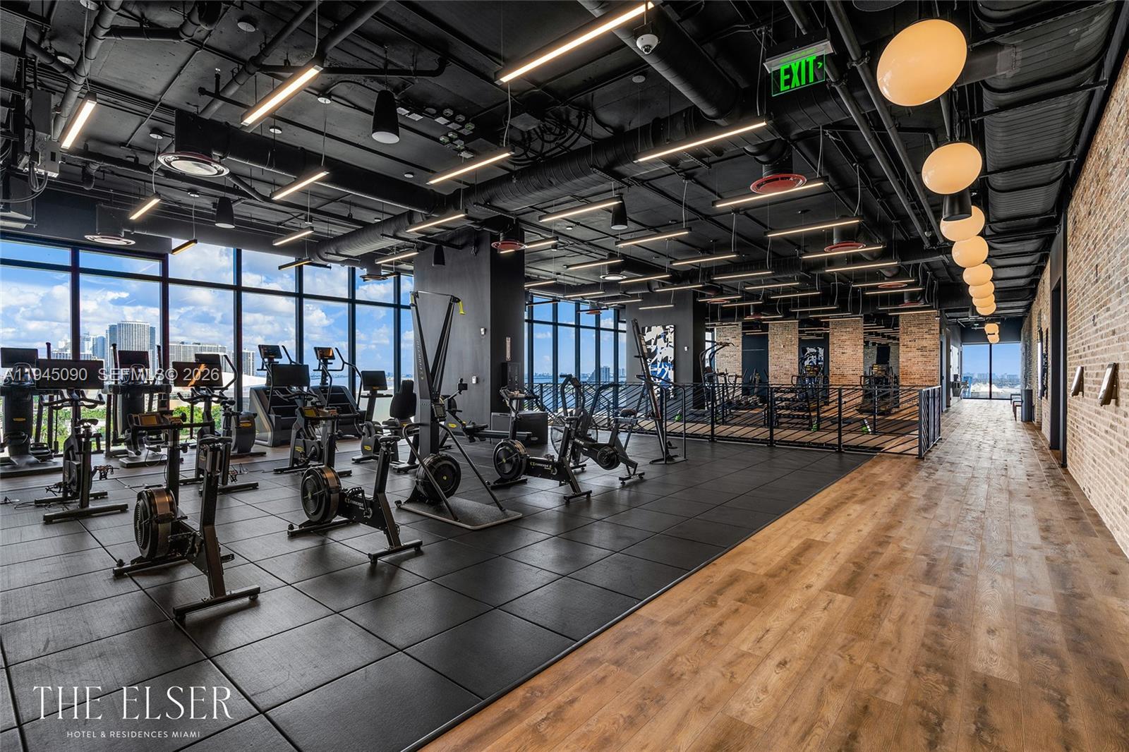 A modern gym features black rubber flooring, wood-look planks, exposed ceilings, and floor-to-ceiling windows — 398 NE 5th St # 1617, Miami FL 33132, MIAMI, FL