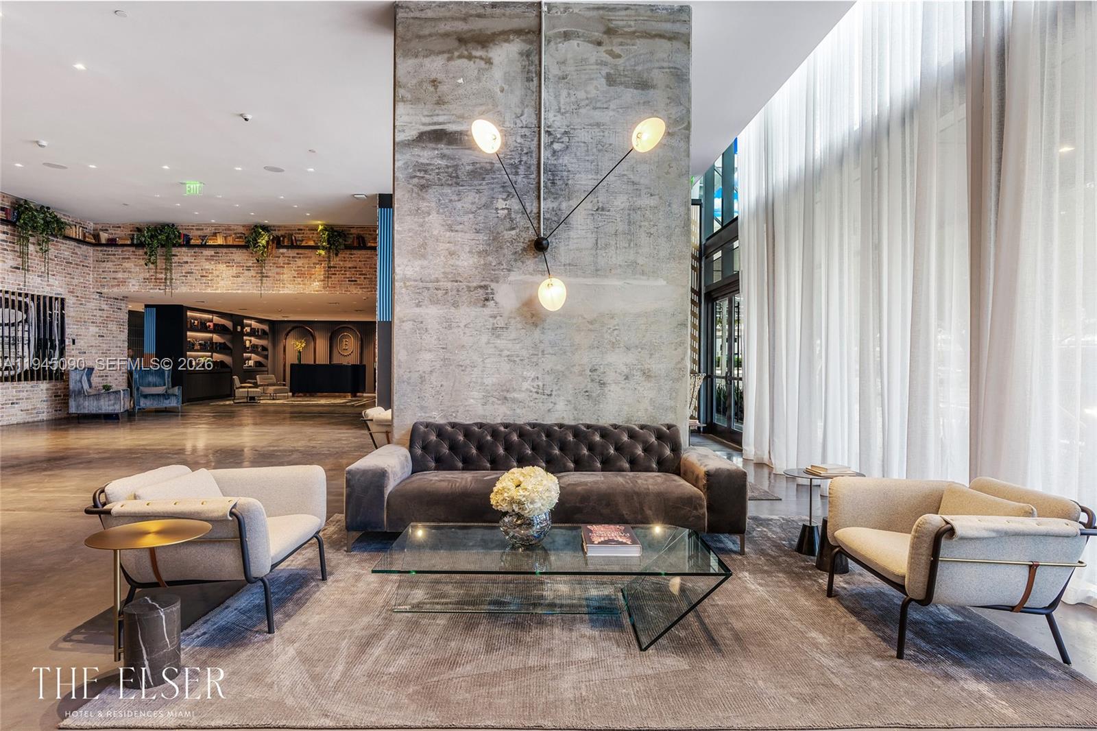 A modern hotel lobby features a tufted sofa, armchairs, and a concrete accent wall — 398 NE 5th St # 1617, Miami FL 33132, MIAMI, FL