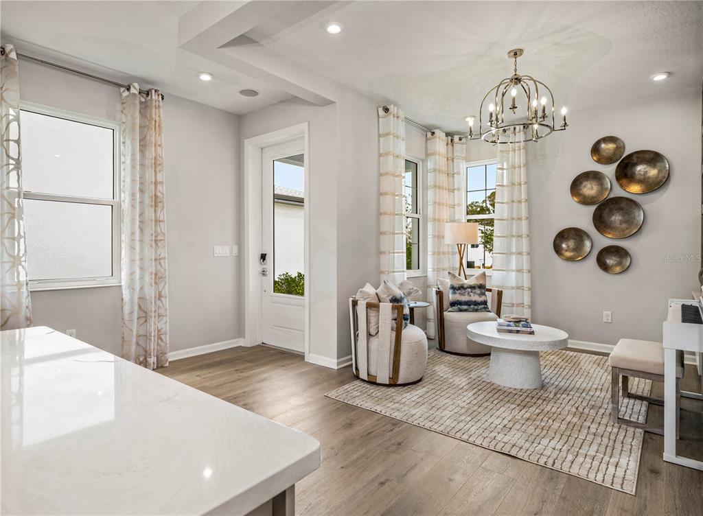 A bright living area features light wood floors, a chandelier, and a circular wall art display — 427 VERONA WAY, LADY LAKE, FL