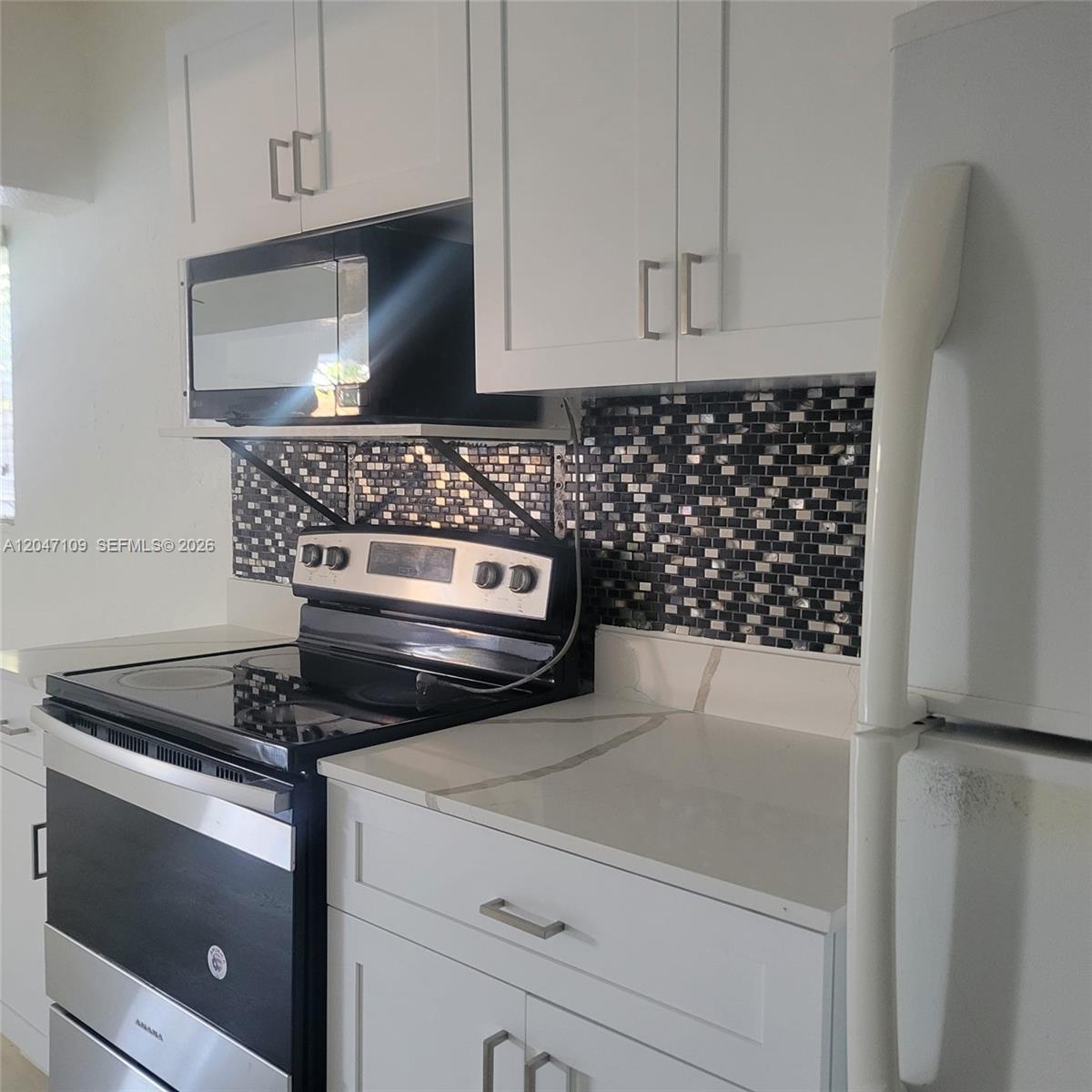 A kitchen features white cabinets, a black stove, a microwave, and a mosaic tile backsplash — 715 SW 6th St # 2, Dania Beach FL 33004, DANIA BEACH, FL