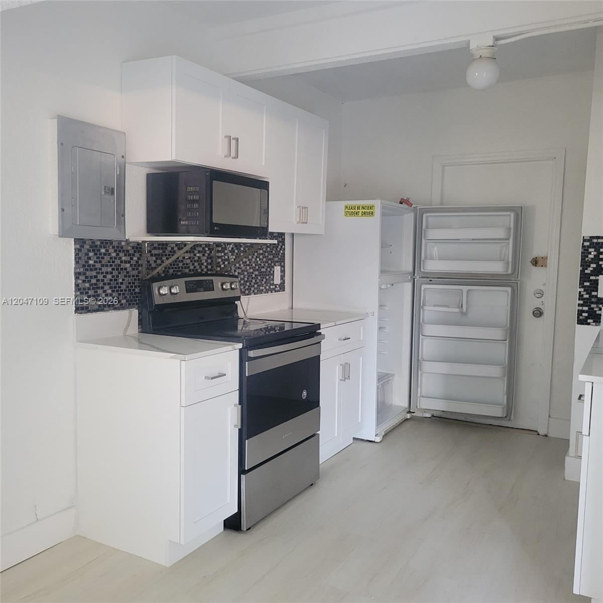 A small kitchen features white cabinets, stainless steel appliances, and a dark mosaic tile backsplash — 715 SW 6th St # 2, Dania Beach FL 33004, DANIA BEACH, FL