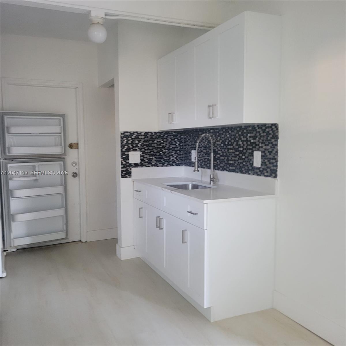 A small kitchen features white cabinets, a stainless steel sink, and a dark mosaic backsplash — 715 SW 6th St # 2, Dania Beach FL 33004, DANIA BEACH, FL