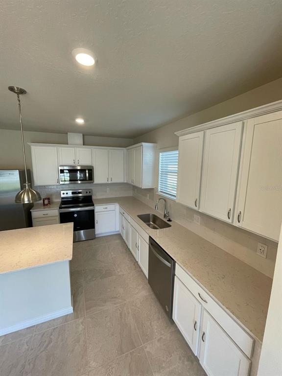 A kitchen features white cabinets, stainless steel appliances, light countertops, and tile flooring — 1926 ENCHANTING COURT, DAVENPORT, FL