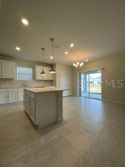 A kitchen with white cabinets, a center island, and tile flooring opens to a living area — 1926 ENCHANTING COURT, DAVENPORT, FL