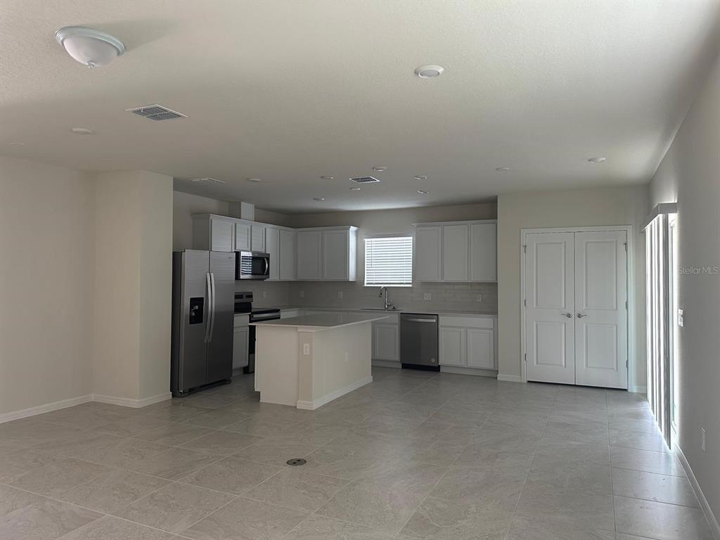 A kitchen with white cabinets, stainless steel appliances, and a central island on tile flooring — 1926 ENCHANTING COURT, DAVENPORT, FL