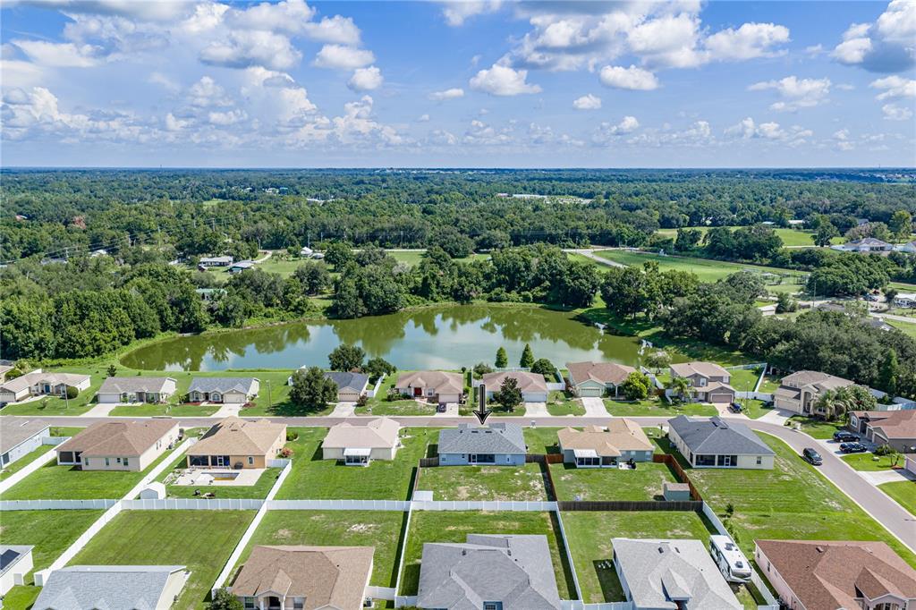 An aerial view shows a suburban neighborhood with houses, fenced backyards, and a central pond — 2734 STONEWOOD DRIVE, LAKELAND, FL