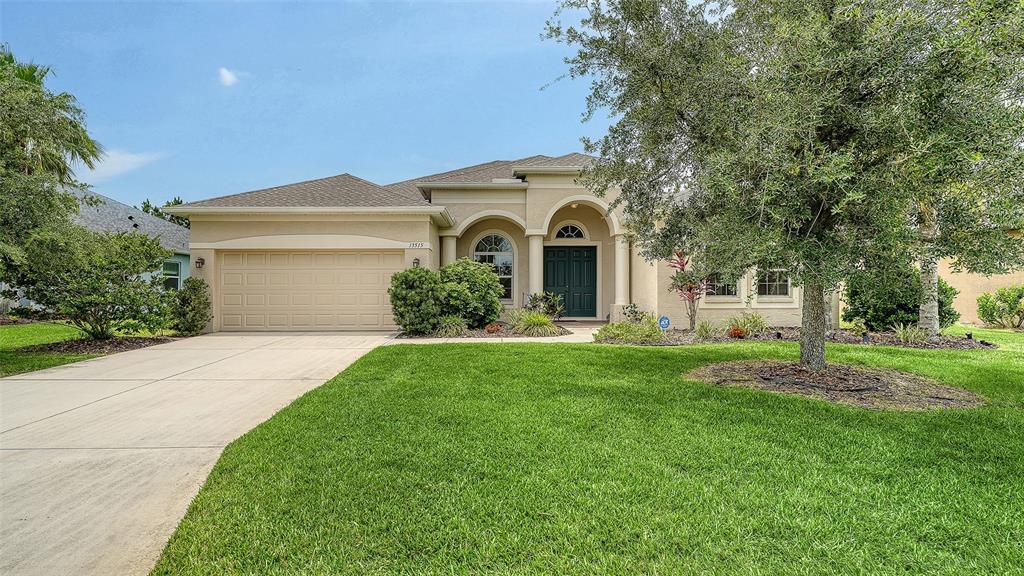 A single-story suburban house features a two-car garage, arched entryway, and a manicured lawn — 13515 22ND COURT E, PARRISH, FL