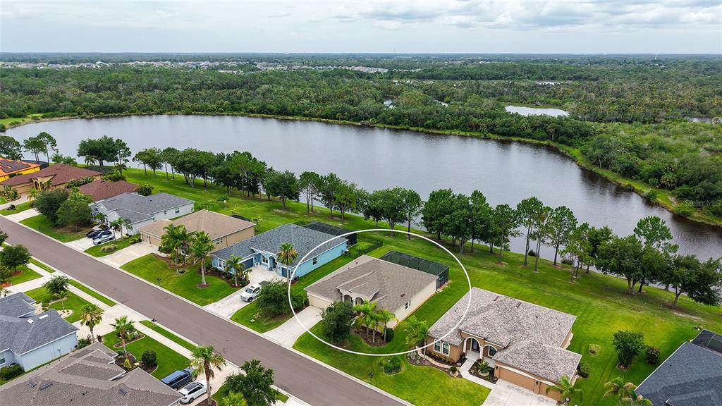 An aerial view shows a suburban house with a screened pool enclosure near a lake — 13515 22ND COURT E, PARRISH, FL