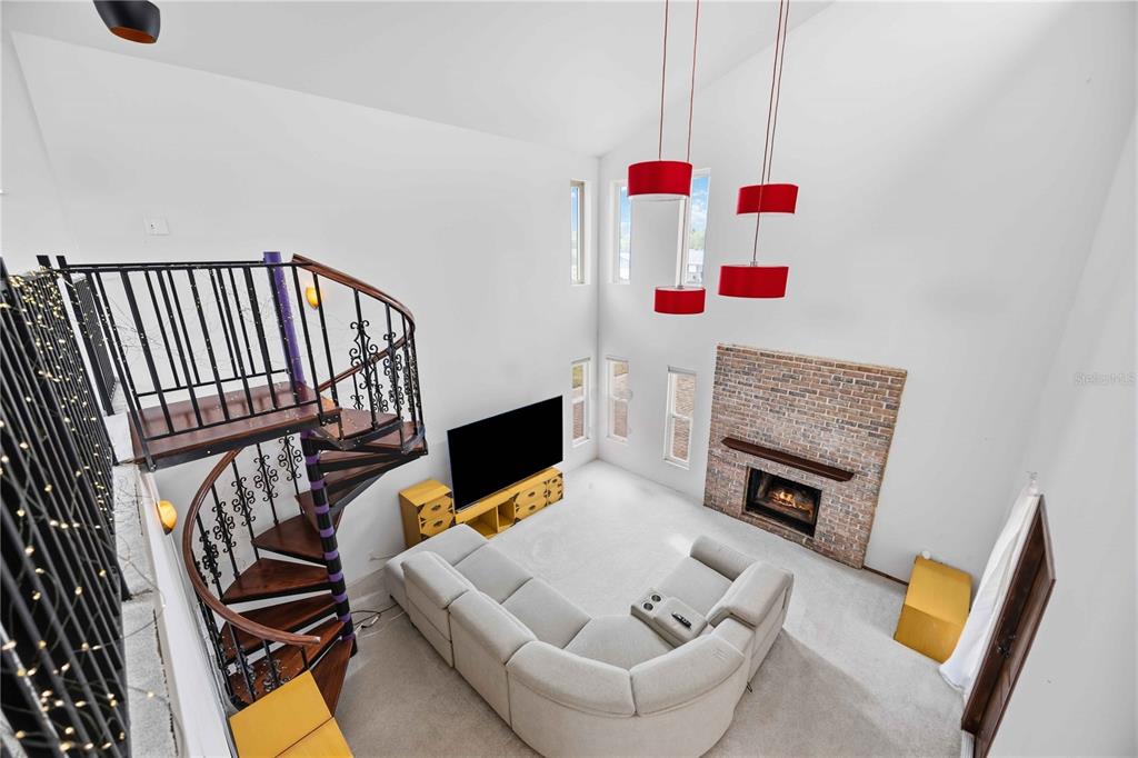 A high-ceiling living room features a spiral staircase, a brick fireplace, and red pendant lights — 6515 MAUNA LOA BOULEVARD, SARASOTA, FL
