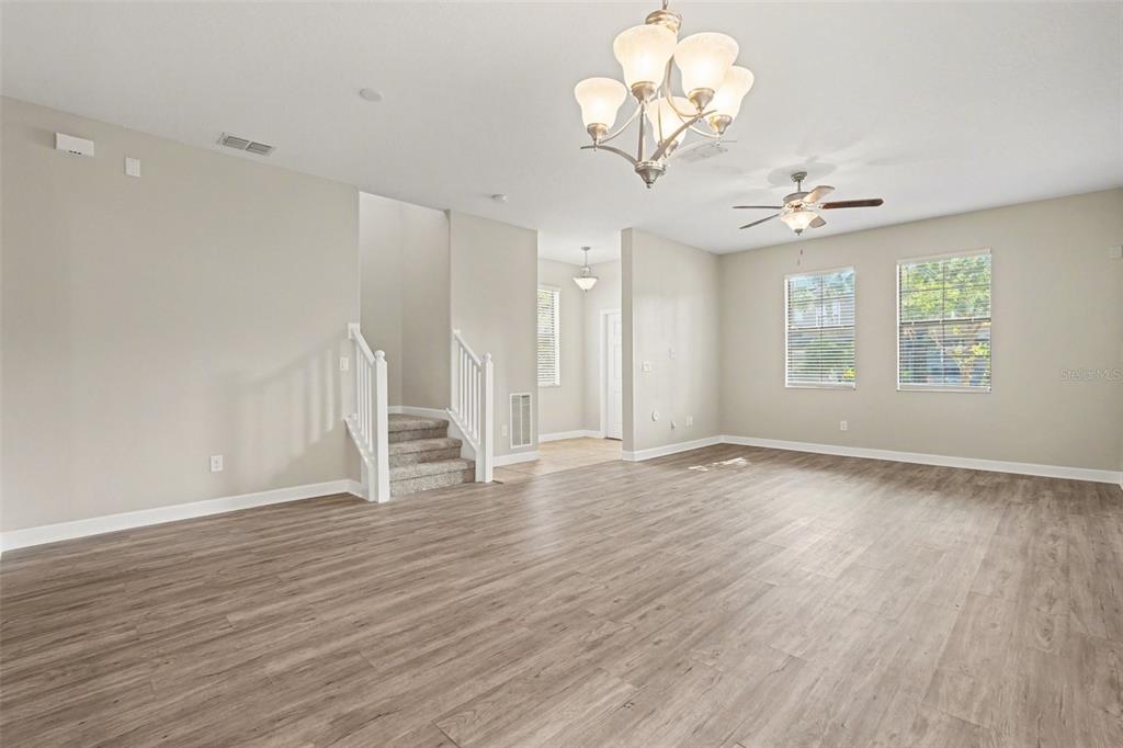 A spacious living room features light wood-look flooring, a chandelier, a ceiling fan, and stairs — 28522 E PLEASANT BAY LOOP, WESLEY CHAPEL, FL