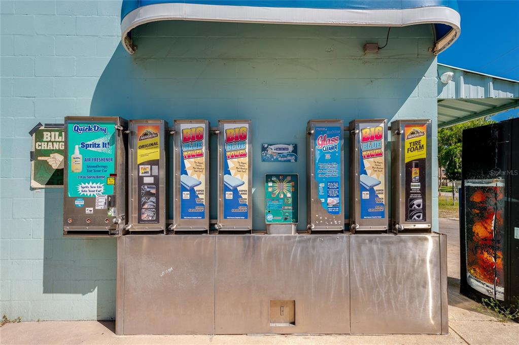 A row of outdoor vending machines for car care products is mounted on a blue wall — 1451 N NOVA ROAD, DAYTONA BEACH, FL