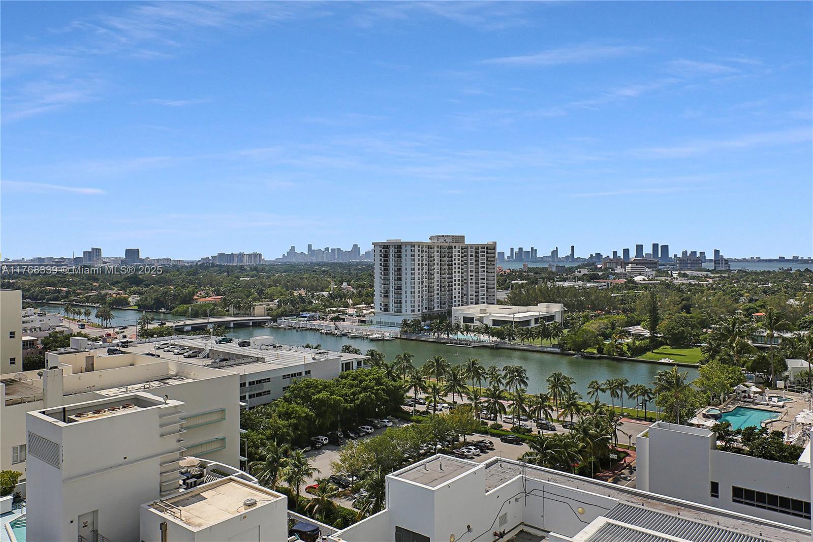 An elevated view shows a canal, palm trees, residential buildings, and a distant city skyline — 4391 Collins Ave # 1415, Miami Beach FL 33140, MIAMI BEACH, FL