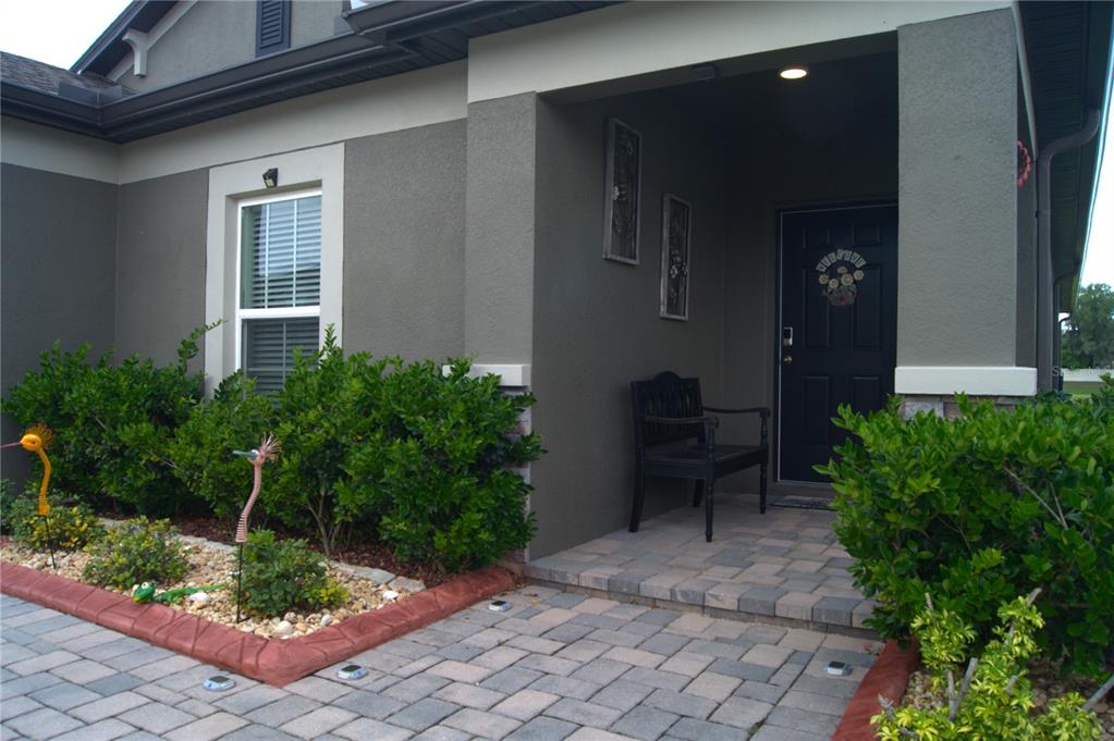 A covered entryway with a black front door, a bench, and a paver walkway — 12407 HILLTOP FARMS DRIVE, DADE CITY, FL