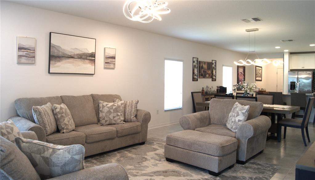 A living room with gray furniture, a patterned area rug, and an adjacent dining area — 12407 HILLTOP FARMS DRIVE, DADE CITY, FL
