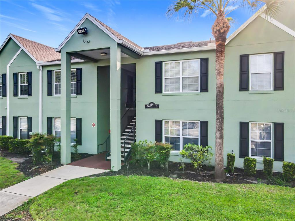 A two-story green apartment building with black shutters and a palm tree in front — 2065 DIXIE BELLE DRIVE UNIT 2065M, ORLANDO, FL