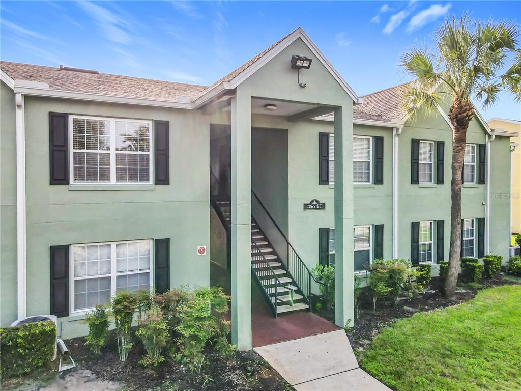A two-story apartment building with green stucco walls, dark shutters, and an exterior staircase — 2065 DIXIE BELLE DRIVE UNIT 2065M, ORLANDO, FL