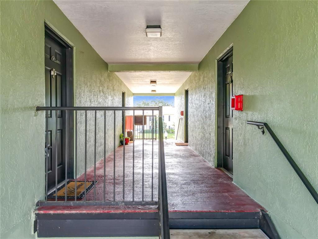 An outdoor apartment hallway with green textured walls, dark doors, and a metal railing — 2065 DIXIE BELLE DRIVE UNIT 2065M, ORLANDO, FL