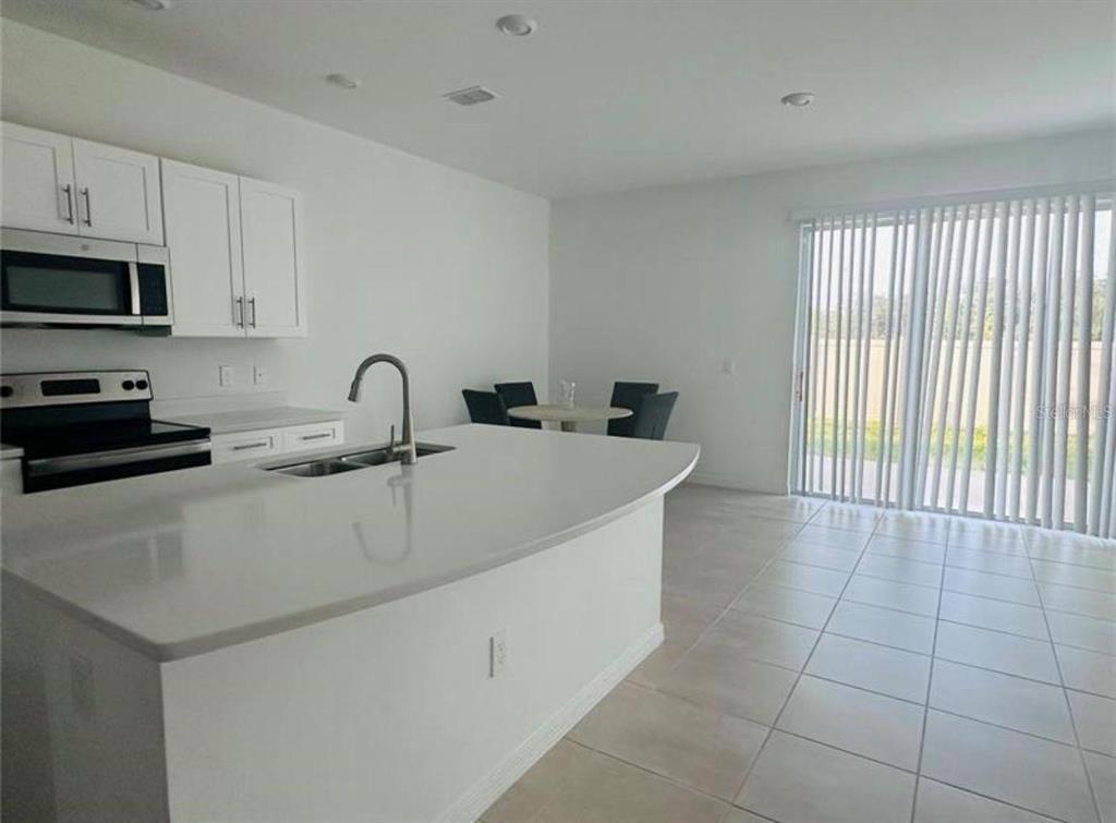 A kitchen with white cabinets, a curved island, and tile flooring opens to a dining area — 4512 TEOLI COURT, KISSIMMEE, FL