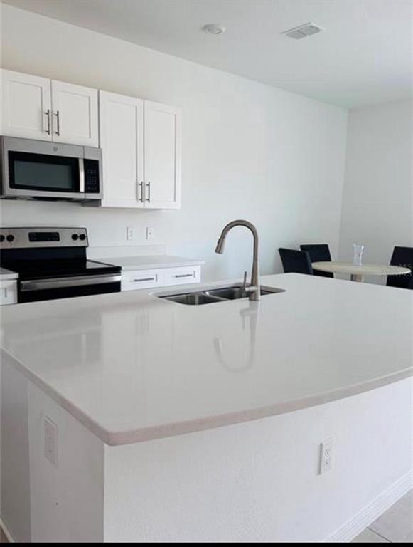 A kitchen features white cabinets, a stainless steel microwave, and a large white island — 4512 TEOLI COURT, KISSIMMEE, FL