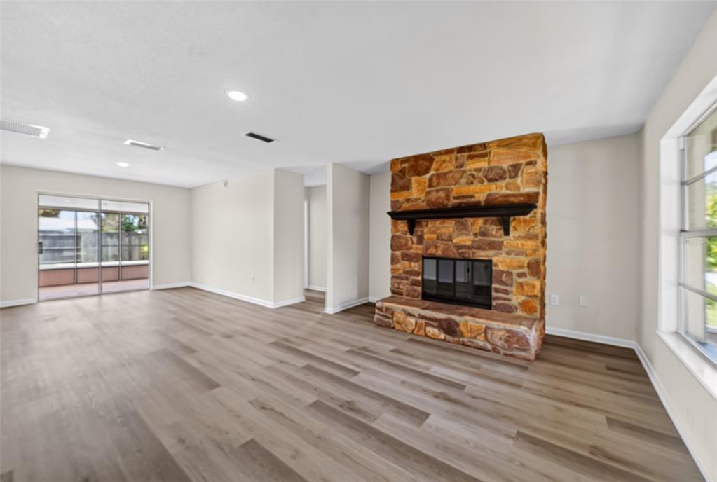 A living room with light wood-look flooring, a stone fireplace, and sliding glass patio doors — 5181 FREDERICK AVENUE, WEST MELBOURNE, FL