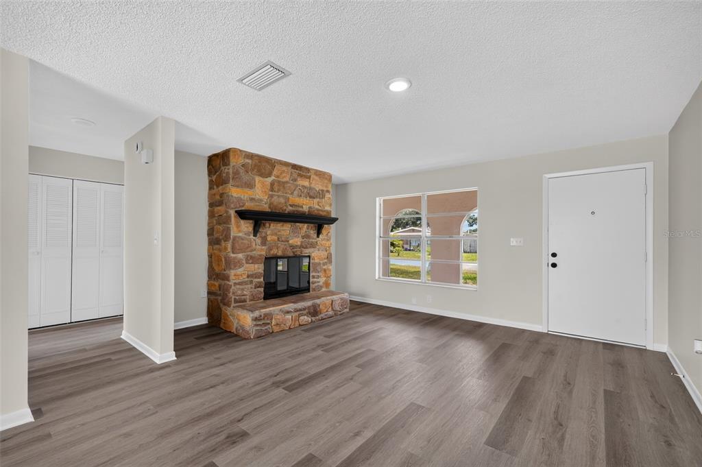 A living room with wood-look flooring, a stone fireplace, and a white front door — 5181 FREDERICK AVENUE, WEST MELBOURNE, FL