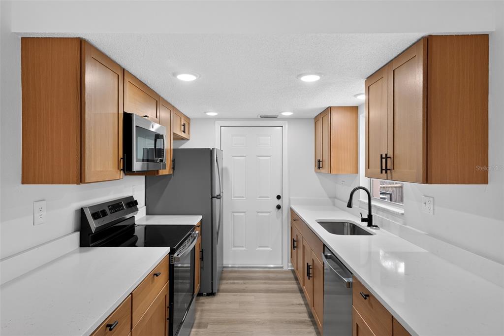 A galley kitchen features wood cabinets, white countertops, stainless steel appliances, and a white door — 5181 FREDERICK AVENUE, WEST MELBOURNE, FL