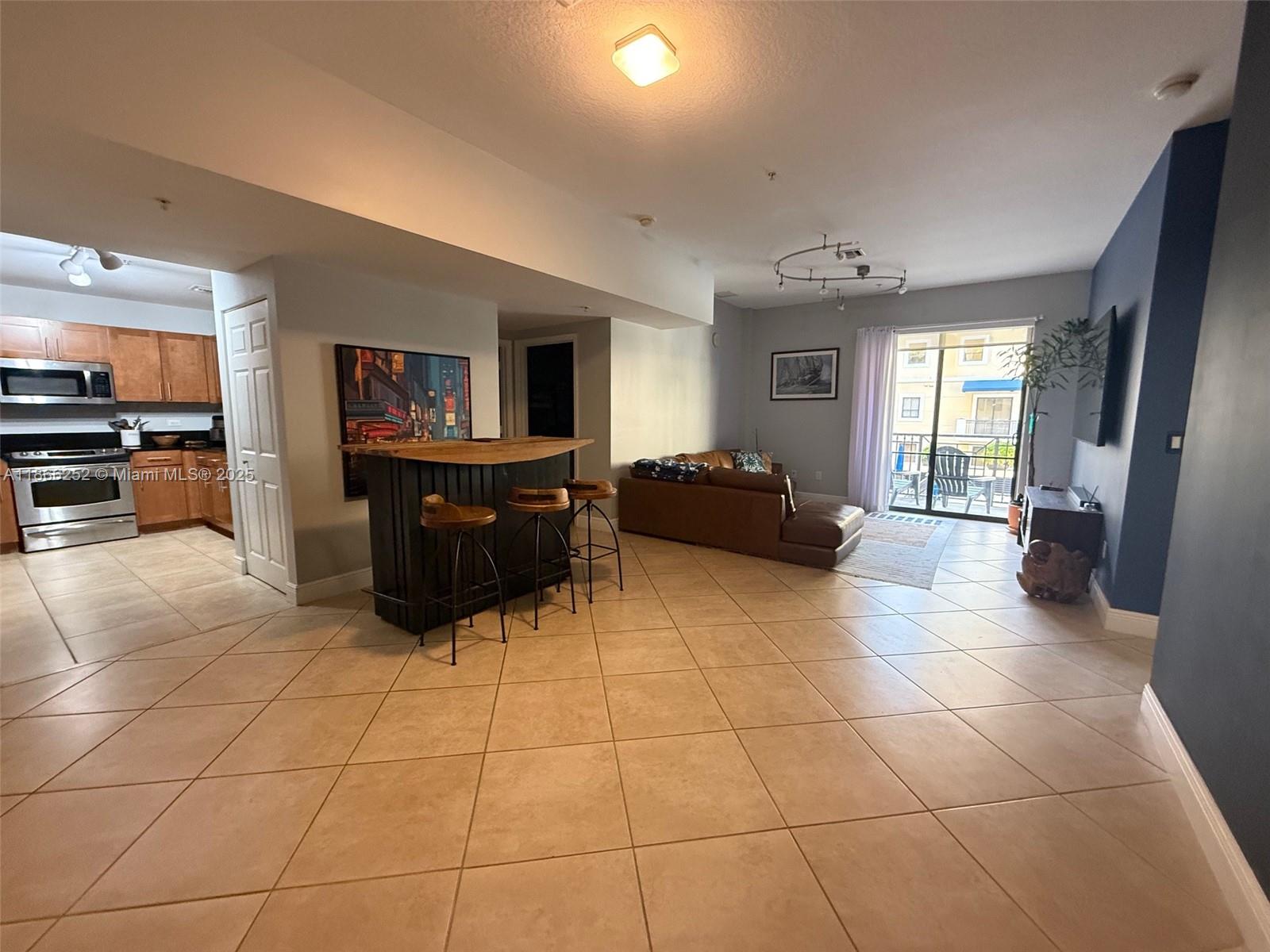 An open-concept living area features a kitchen, a bar with stools, and a balcony view — 8395 SW 73rd Ave # 509, Miami FL 33143, MIAMI, FL