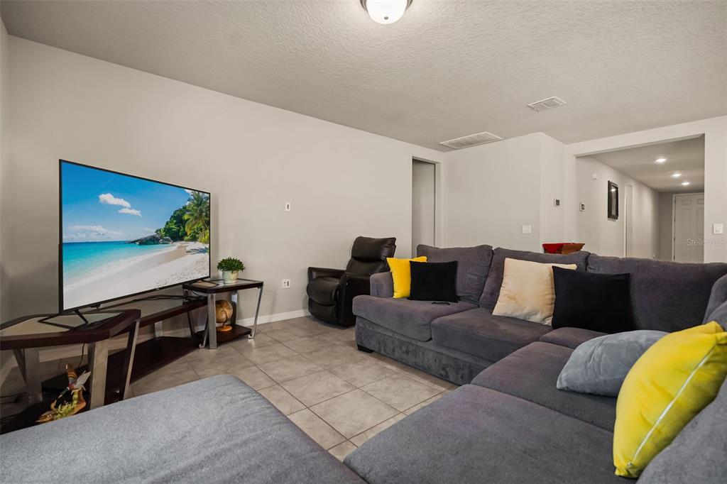 A living room features a large television, a gray sectional sofa, and tile flooring — 1166 YUMURI STREET, WINTER HAVEN, FL