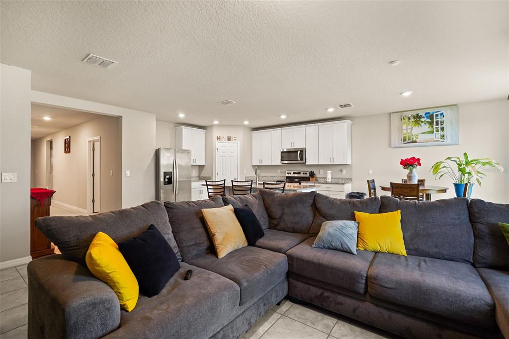 A spacious open-concept living room features a large gray sectional sofa facing a white kitchen — 1166 YUMURI STREET, WINTER HAVEN, FL