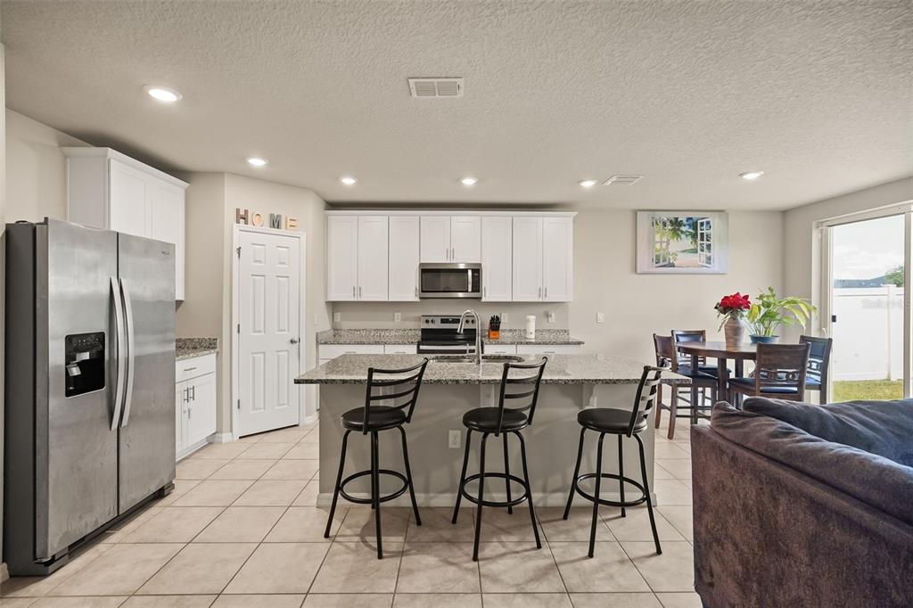 A kitchen features white cabinets, granite countertops, a center island with bar seating, and stainless appliances — 1166 YUMURI STREET, WINTER HAVEN, FL
