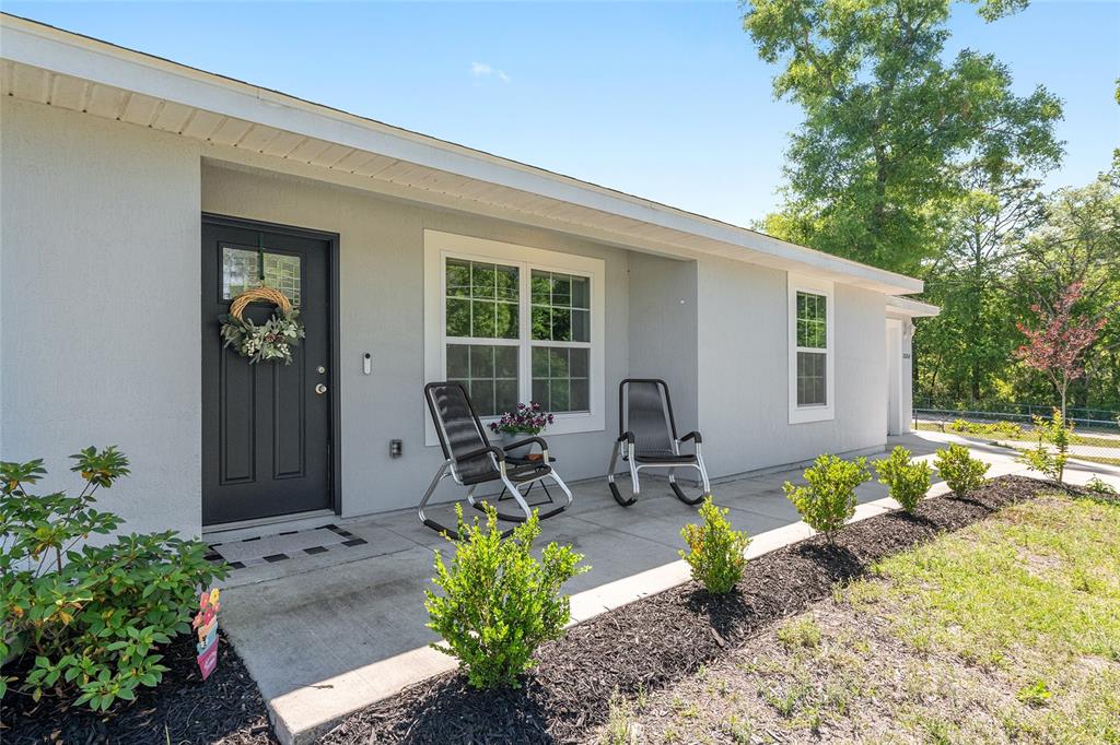 A light gray house exterior features a dark front door, a concrete porch, and landscaping — 20264 SW 69TH PLACE, DUNNELLON, FL