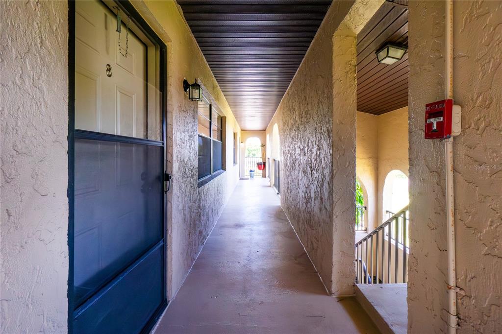 An outdoor apartment hallway features a textured wall, a screen door, and a fire alarm — 1217 AQUI ESTA DRIVE UNIT 8, PUNTA GORDA, FL
