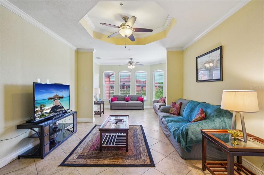 A living room features a tray ceiling, tile flooring, two sofas, and a television console — 2713 VIA MURANO UNIT 233, CLEARWATER, FL