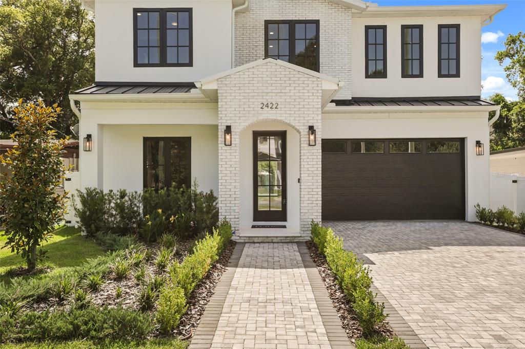A two-story house with white stucco, brick accents, black-framed windows, and a paved walkway — 2422 MUSSELWHITE AVENUE, ORLANDO, FL