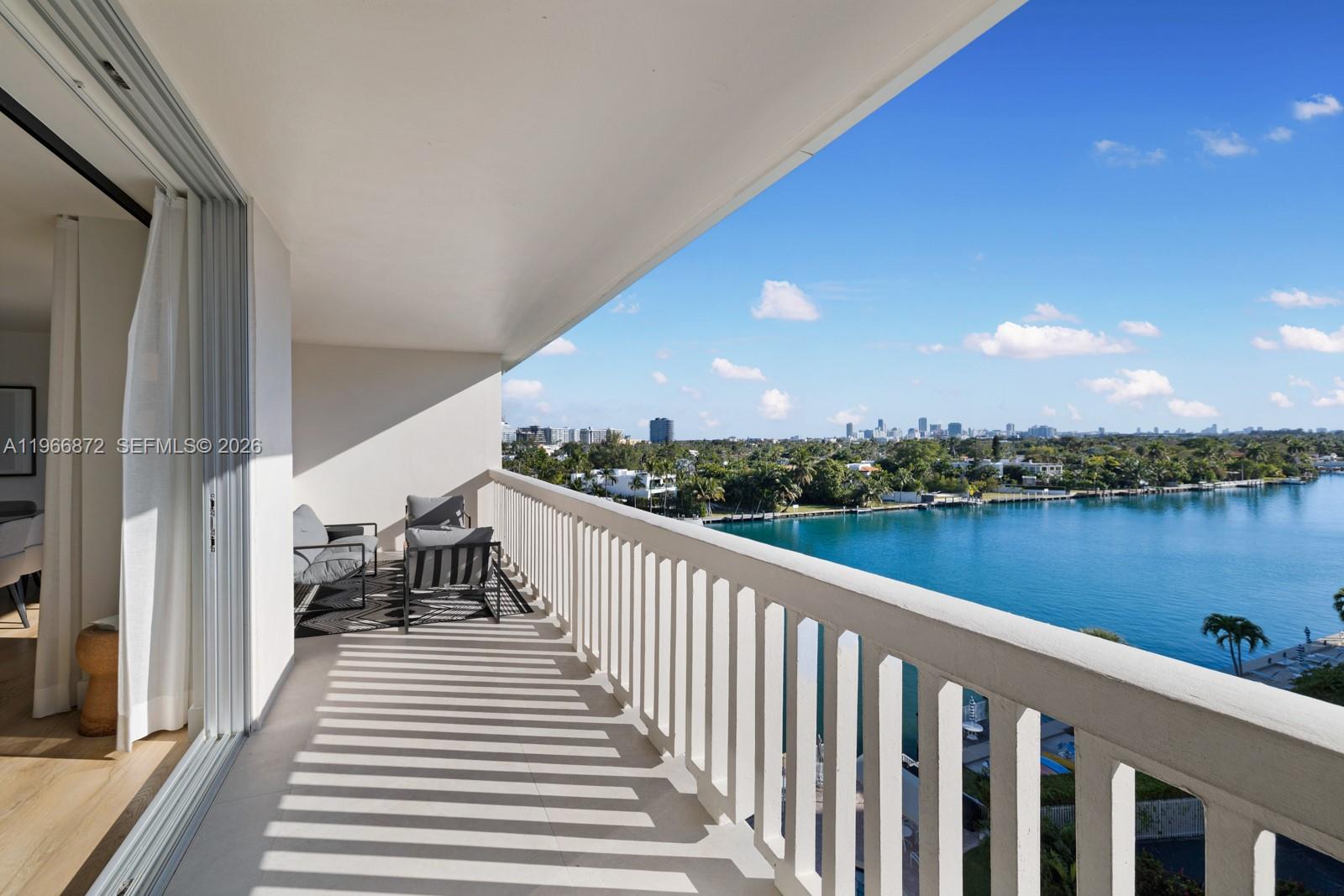 A balcony with a white railing overlooks a body of water and a distant city skyline — 9111 E Bay Harbor Dr # D, Bay Harbor Islands FL 33154, BAY HARBOR ISLANDS, FL
