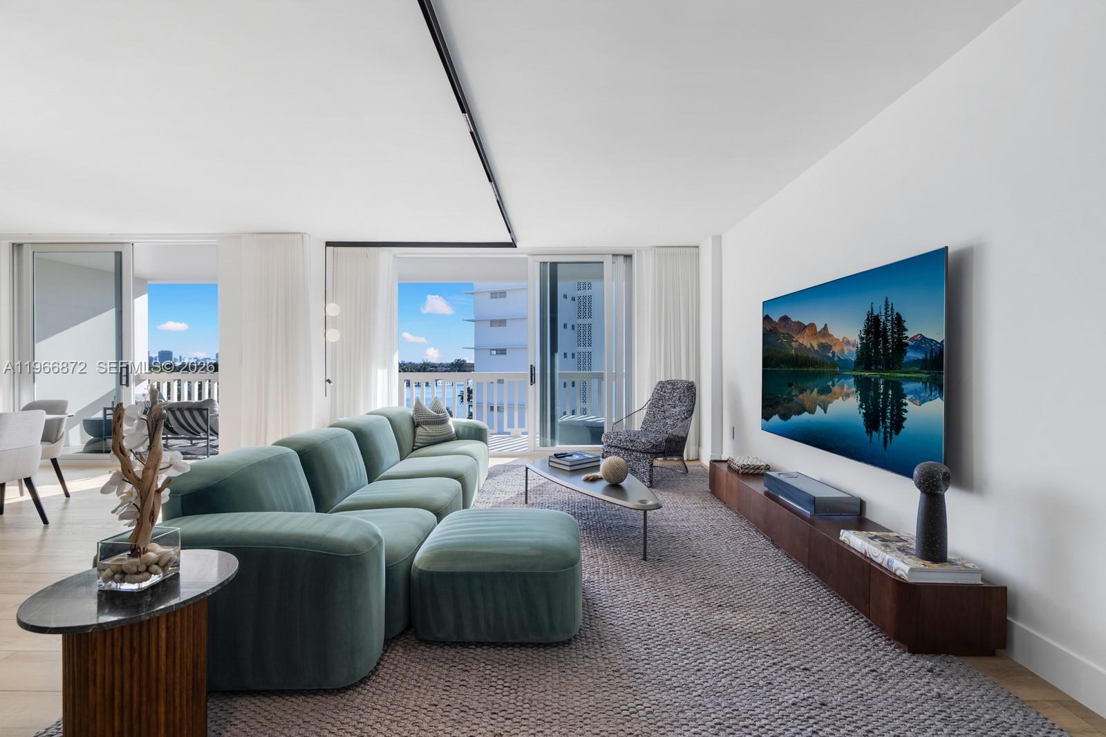 A modern living room features a green sectional sofa, a wall-mounted television, and balcony views — 9111 E Bay Harbor Dr # D, Bay Harbor Islands FL 33154, BAY HARBOR ISLANDS, FL