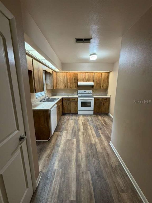 A galley kitchen features wood cabinets, light countertops, and wood-look flooring — 2366 LAKE DRIVE NW, WINTER HAVEN, FL